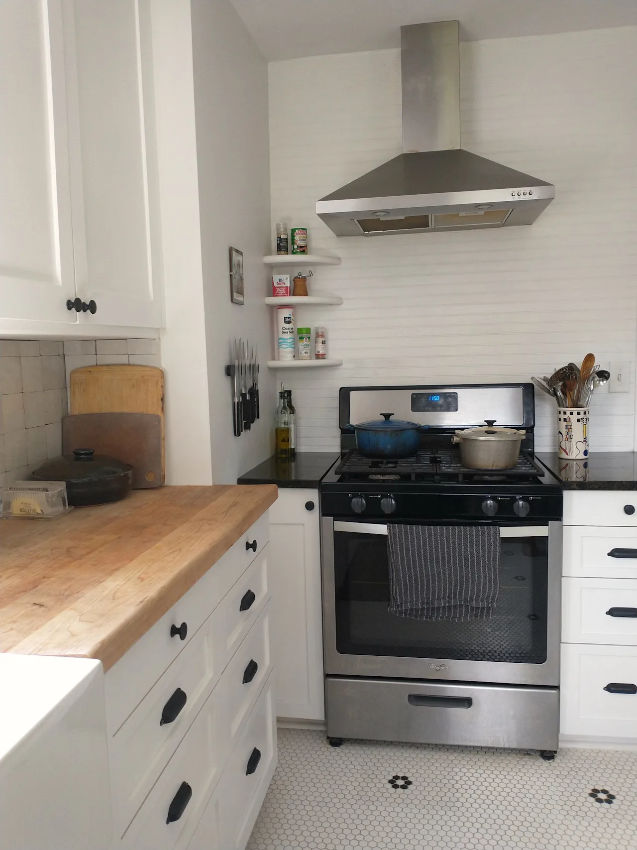 Kitchen with white cabinets, a butcher-block counter, a stainless range and vent hood, and open shelving.