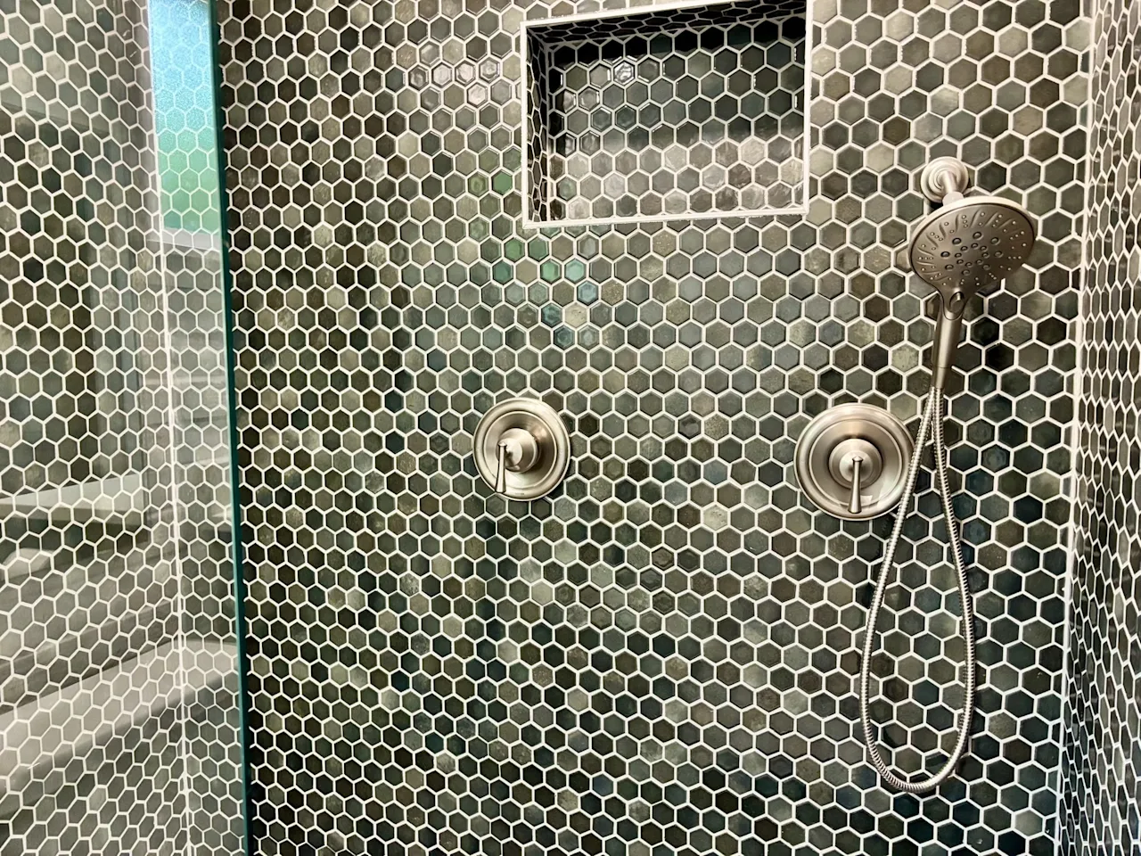 Close-up of the green penny-tile shower wall with a recessed niche and brushed-nickel fixtures.