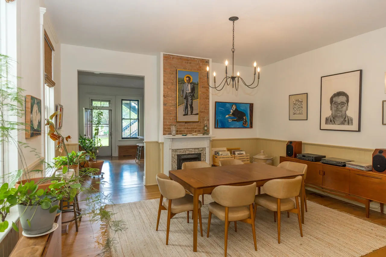 Open dining room with a wood table and mid-century chairs, a brass chandelier, a gallery wall of portraits, and a fireplace.