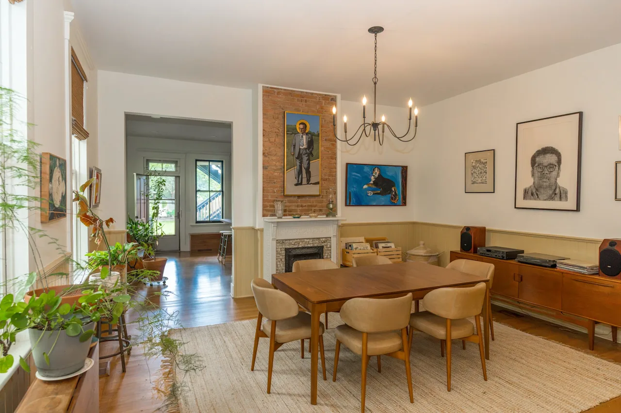 Open dining room with a wood table and mid-century chairs, a brass chandelier, a gallery wall of portraits, and a fireplace.