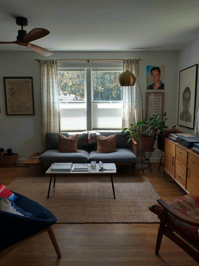 The living room post-renovation with refinished floors, mid century furniture, custom art, and plenty of sunlight.