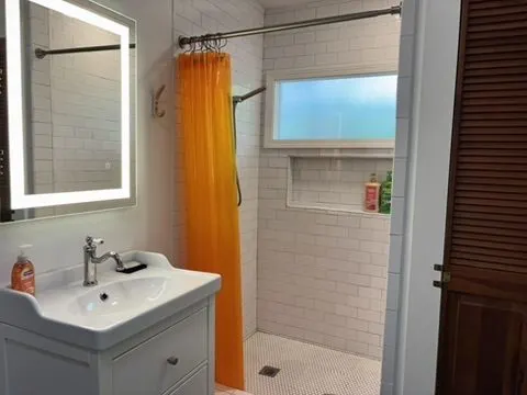 Bathroom vanity with an LED mirror, a white subway-tile walk-in shower, and an orange shower curtain.