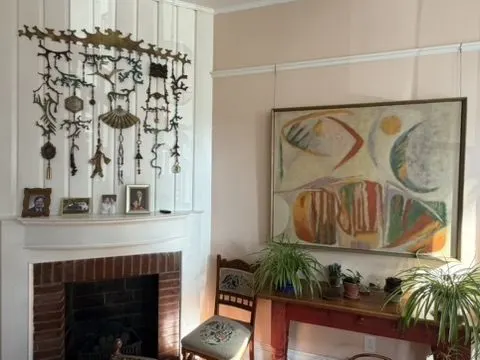 Living room with a brick fireplace, an abstract painting, an antique console table, and a collection of hanging ornaments.
