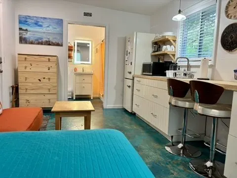 Studio with a blue-stained concrete floor, light cabinetry, a breakfast bar with stools, and a view to the bathroom.