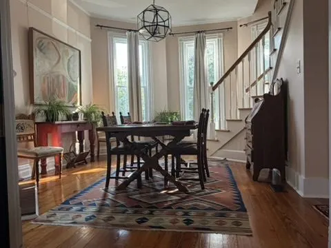 Elegant dining room with a wood table, a patterned area rug, an antique secretary desk, and a staircase in a bay-window space.