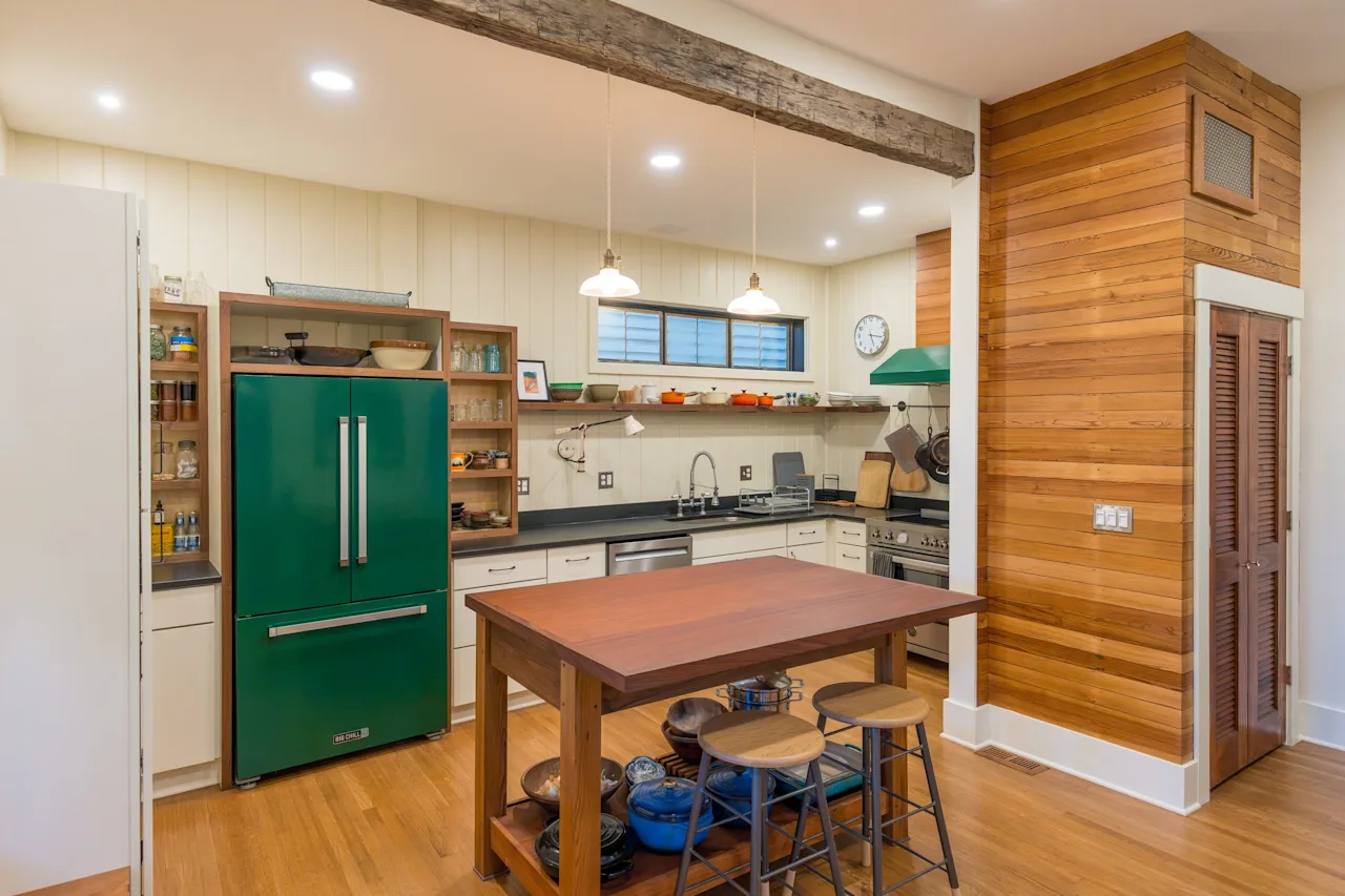 Renovated kitchen with a green retro-style refrigerator, cedar accent wall, butcher-block island with stools, and a reclaimed ceiling beam.