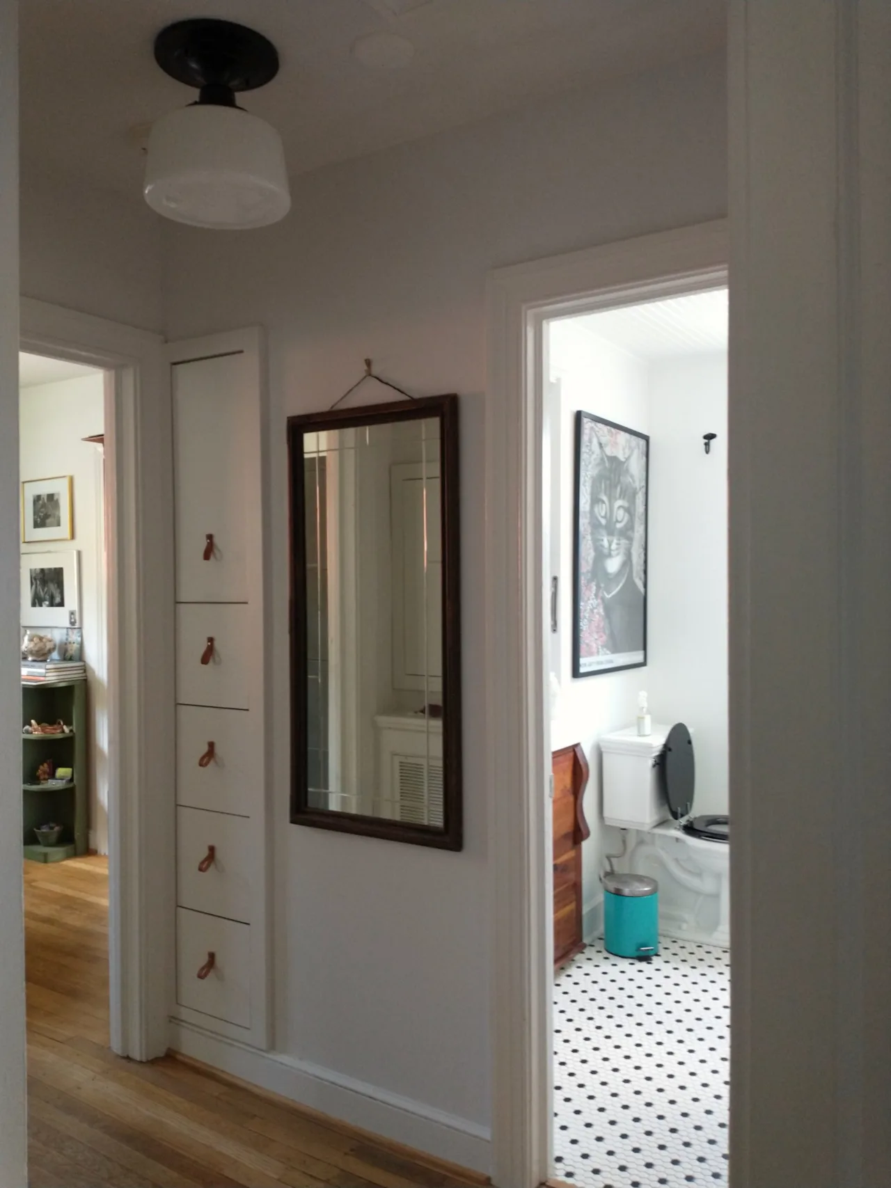 Hallway view with a wood-framed mirror over a built-in dresser, looking through to a black-and-white tiled bathroom.