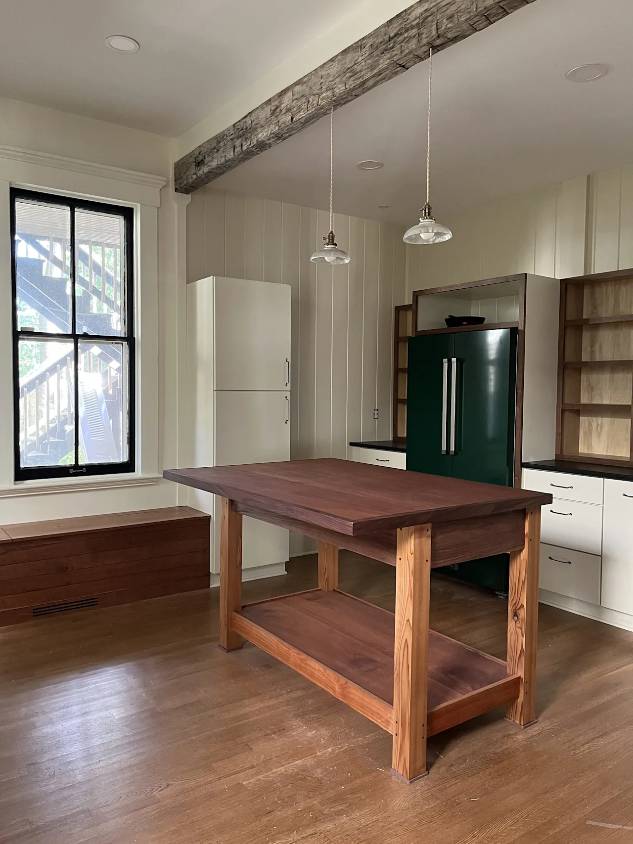 Renovated kitchen in the Highlands Victorian with a green refrigerator, a reclaimed-wood island, a rustic ceiling beam, pendant lights, and tall windows.