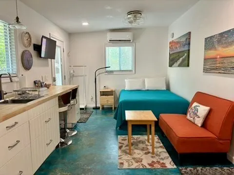 Studio living space with a teal-covered bed, an orange loveseat, a desk workspace, and a wall-mounted TV.