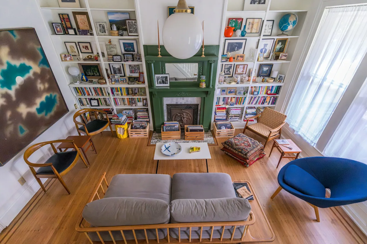 Book-lined living room with floor-to-ceiling shelves, a green fireplace, a low sofa, and a blue accent chair on hardwood floors.
