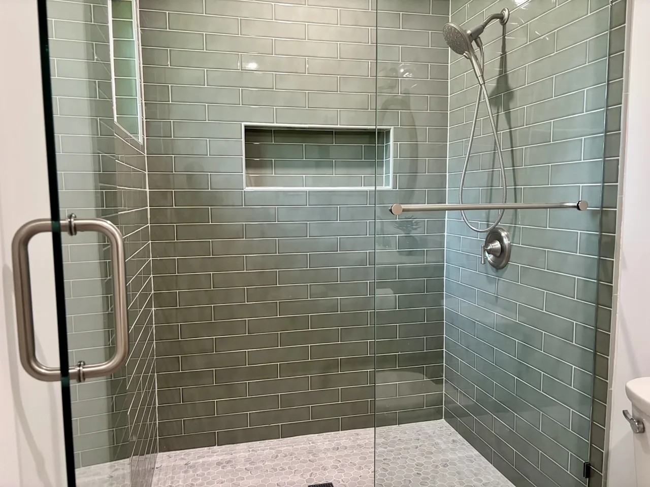 Glass walk-in shower with grey-green subway tile, a recessed niche, and a tiled bench.