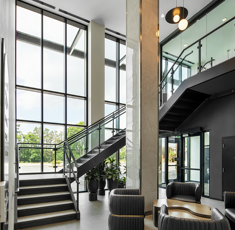 The Carrick's sophisticated lobby with two storey windows, glass-railing central stairs, and lounge space. 