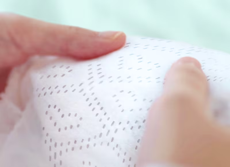 A close-up shot shows two hands gently holding a soft-textured Pampers nappy, highlighting its dotted pattern and plush feel A close-up shot shows two hands gently holding a soft-textured Pampers nappy, highlighting its dotted pattern and plush feel
