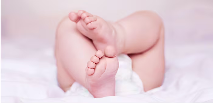 Bose stópki i nóżki noworodka w pieluszce, leżącego na miękkim kocyku - materiały i bezpieczeństwo pieluszek Pampers