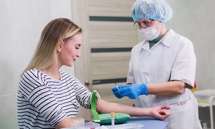 Medizinische Fachkraft bereitet eine Blutabnahme am Arm einer jungen Frau vor – Vorsorgeuntersuchung in der Schwangerschaft