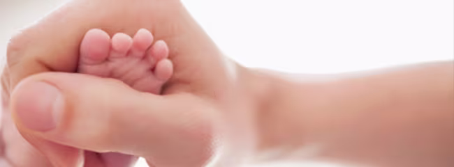 Prim-plan cu piciorul unui nou-născut ținut în palma unui adult