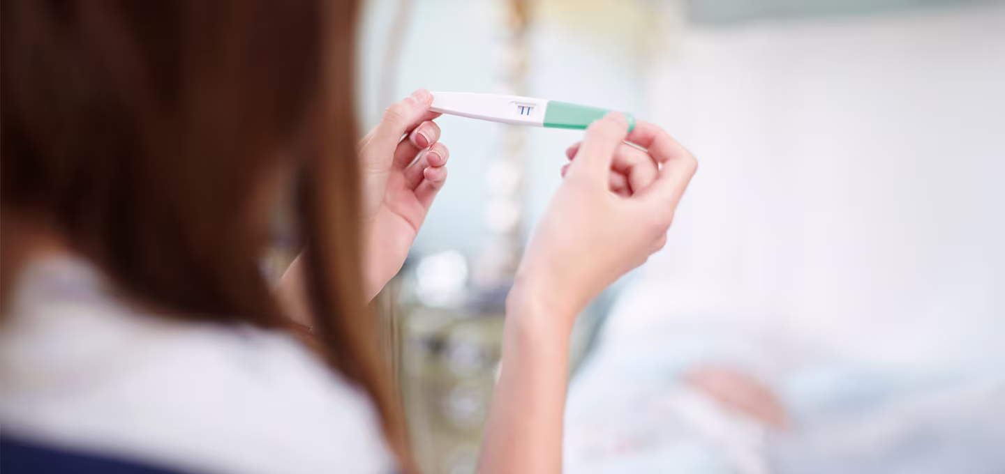 Personne tenant un test de grossesse entre ses mains dans une pièce lumineuse