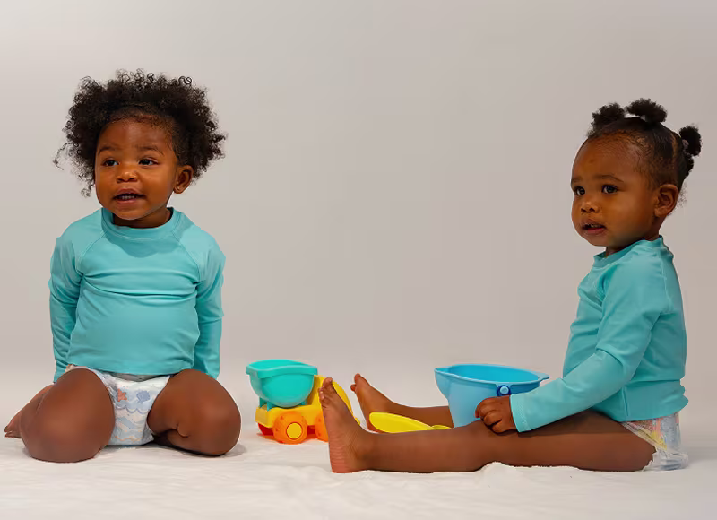 Two toddlers wearing Pampers Splashers, sit together with some colorful toys Two toddlers wearing Pampers Splashers, sit together with some colorful toys
