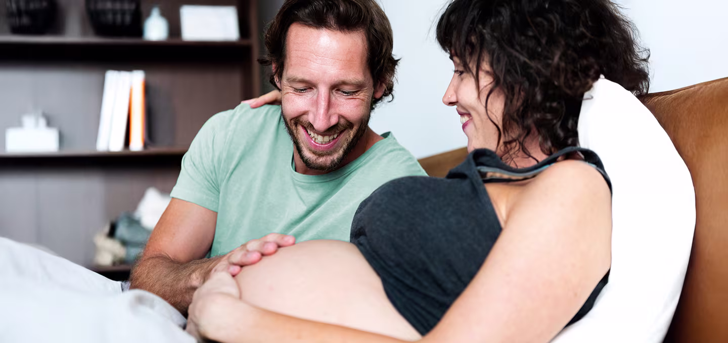 Pareja sonriente en casa, el hombre toca con cariño el vientre de la mujer embarazada.