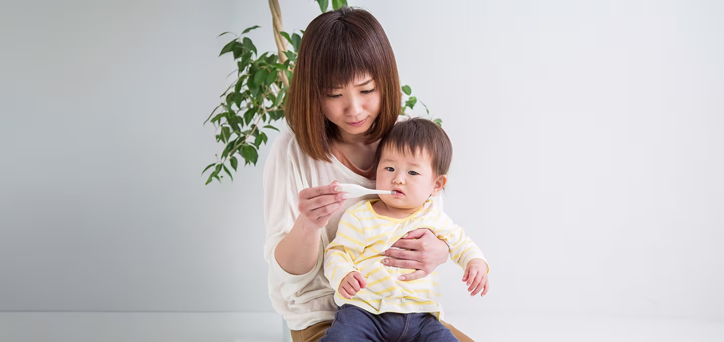 Madre sentada sostiene a su bebé mientras le ofrece una cucharada de líquido, ilustrando cuidado y alimentación durante un episodio de diarrea infantil.