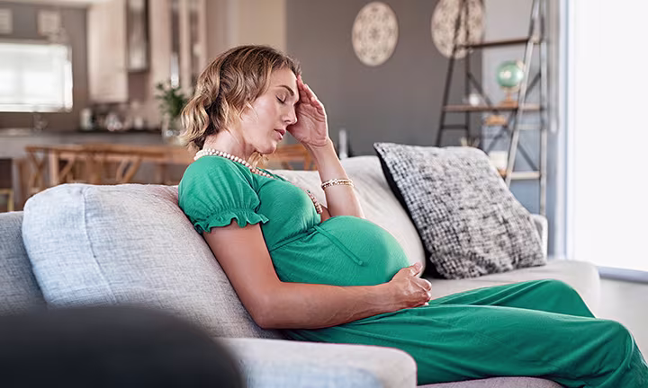 Schwangere Frau mit Eisenmangel sitzt auf Couch