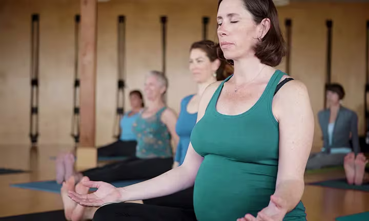 Schwangere Frau praktiziert Meditation in einem Schwangerschafts-Yogakurs mit anderen Teilnehmerinnen in einem Studio