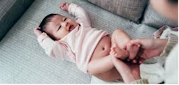 Adulte changeant la couche d’un bébé allongé sur une surface douce tandis que le bébé bouge les jambes.