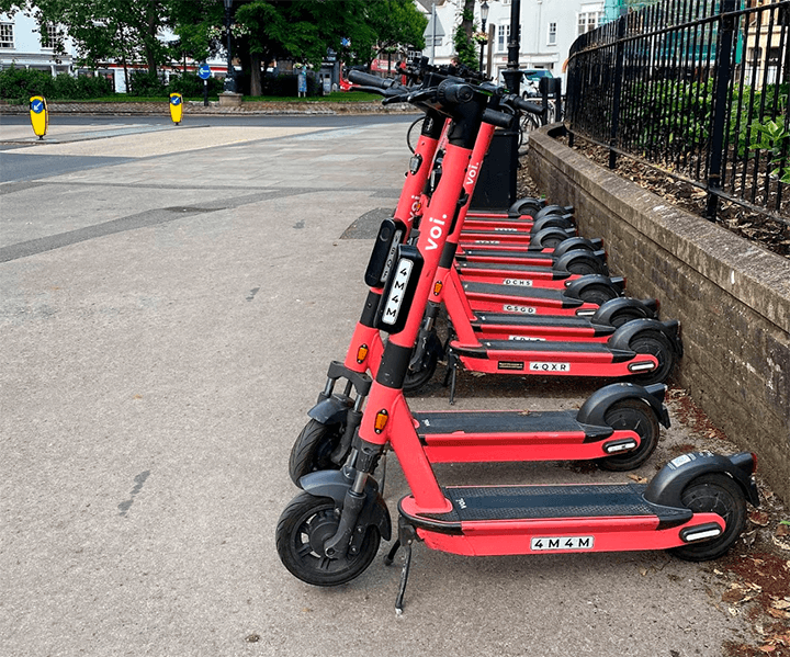 A row of several electric scooters parked together on the pavement.