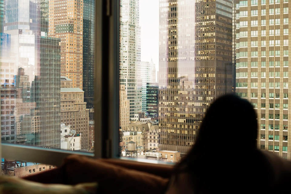 High-rise buildings seen through a window, with a seated person silhouetted in the foreground.