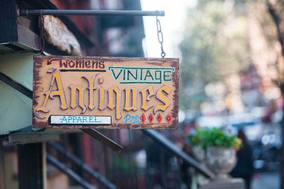 Weathered hanging sign advertising women's vintage antiques and apparel from before 1960.