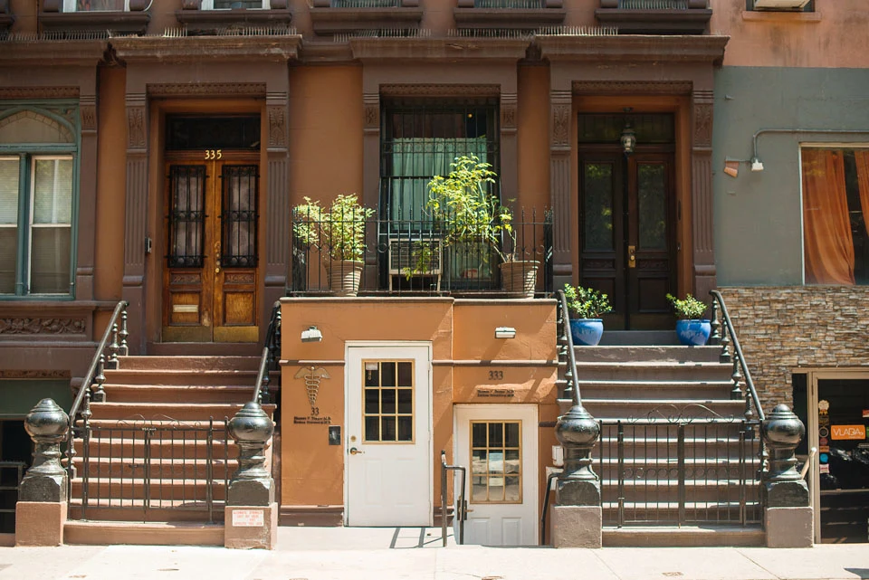 Attached brownstones with raised stoops, iron railings, and planted terraces.