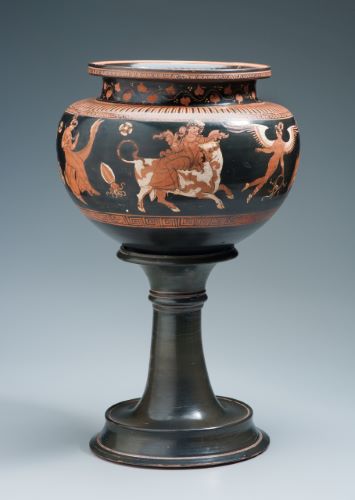 A round bowl sits on a tall narrow base. The base is painted black, but a procession of figures wraps around the upper bowl. Led by a winged figure, a woman is seated on a bi-colored bull.  She is followed by another woman riding on a dolphin. 