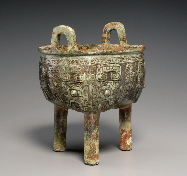 Bronze three-lobed bowl with three tubular legs and two "u"-shaped handles on the rim.