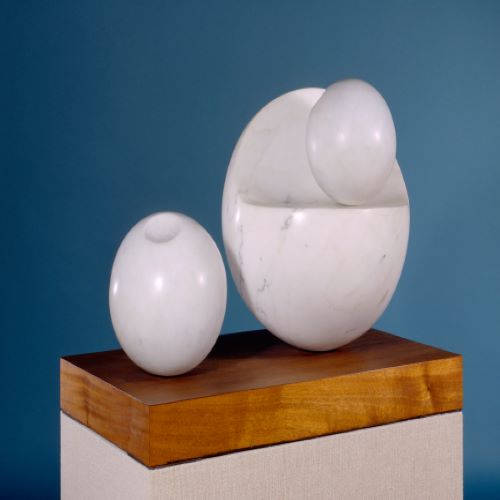 Three white marble spheres, the smallest nesting in the concave curve of the largest. The third sphere sits to the left and has a small circular depression at its top. The spheres are mounted on a rectangular wooden base.