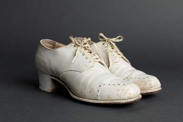 A pair of white low heels with white laces. The shoes appear worn and slightly scuffed, and there are brownish-colored dots staining the toe and side of the white shoes.