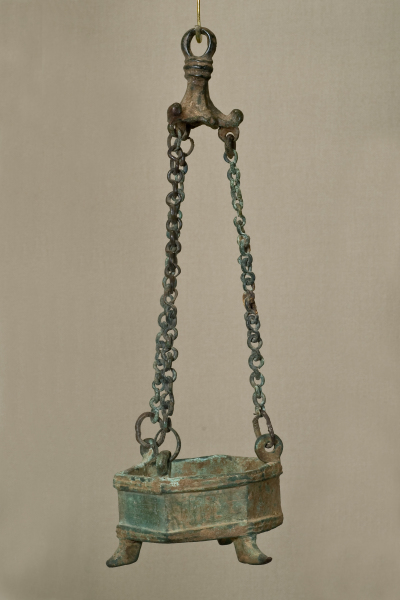 A hexagonal censer with three pointed feet, suspended by three chains attached to a conical finial at the top. The finial has three knobbed, flaring sections with loops below for the chains.