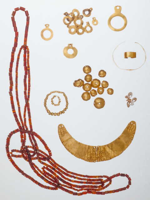 A group of jewelry that includes a gold, crescent-shaped breast ornament, three bead necklaces, a bracelet, a ring, open circular attachments, convex disk attachments, and a selection of beads.