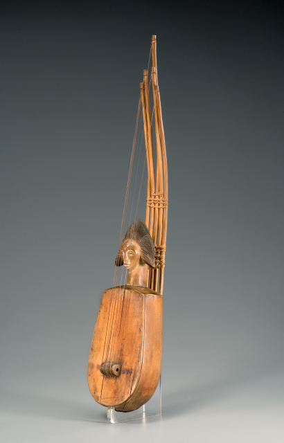 A lightly colored, wooden string instrument. Five rods extend upwards from the instruments smooth, oval body. Thin stings stretch from the tip of each rod to center of the instrument's body. A long neck and head appear at the base of the rods.