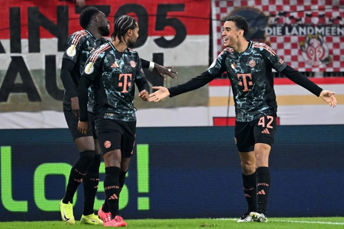 Bayern Munich's German midfielder #42 Jamal Musiala (R) celebrates scoring the first goal with Bayern Munich's German forward #07 Serge Gnabry (C) and Bayern Munich's Canadian defender #19 Alphonso Davies during the German Cup (DFB Pokal) second round football match between 1 FSV Mainz 05 and FC Bayern Munich, in Mainz, western Germany on October 30, 2024.   Kirill KUDRYAVTSEV / AFP