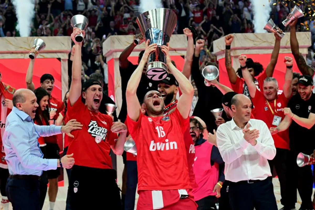Olympiacos' Greek forward #16 Kostas Papanikolaou (C) raises the winners trophy as he celebrates with team mates and staff after winning the men's EuroLeague final basketball match between Olympiacos Piraeus and Real Madrid at the Telekom Center Athens in Athens on May 24, 2026. Angelos Tzortzinis / AFP