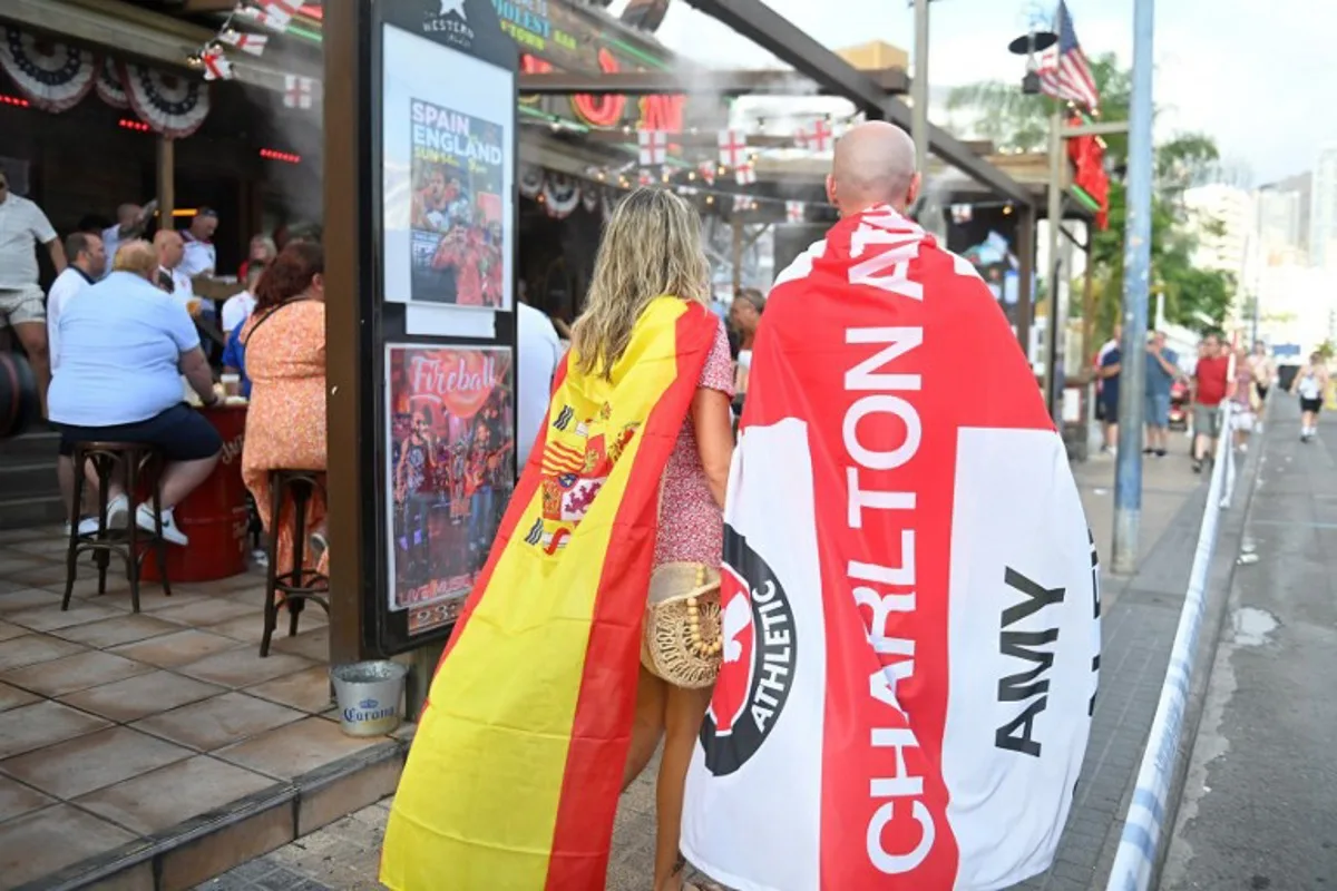 Fans wrapped in England's Charlton Athletic Football Club and Spain's flags walk prior the UEFA Euro 2024 finale football match between Spain and England, in Benidorm, eastern coast of Spain, on July 14, 2024. JOSE JORDAN / AFP
