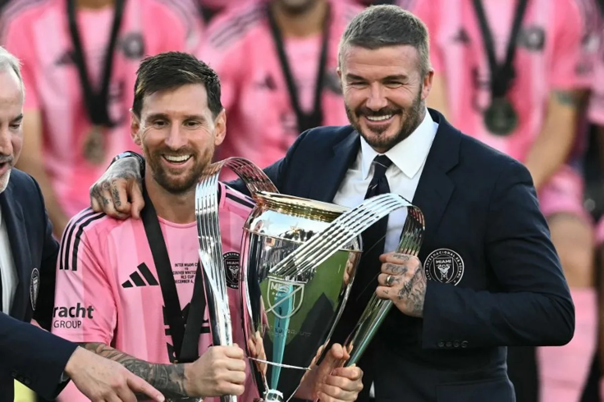 Inter Miami's Argentine forward #10 Lionel Messi (L) poses with the trophy next to the team's owner David Beckham (R) after winning the Major League Soccer (MLS) Cup final between Inter Miami and the Vancouver Whitecaps at Chase Stadium in Fort Lauderdale, Florida, on December 6, 2025. CHANDAN KHANNA / AFP