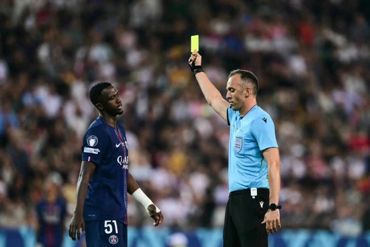 Portuguese referee Joao Pinheiro (R) shows Paris Saint-Germain's Ecuadoran defender #51 Willian Pacho (L) a yellow card as he books him for a foul during the 2025 UEFA Super Cup final football match between Paris Saint-Germain (FRA) and Tottenham Hotspur FC (ENG) at the Friuli stadium, in Udine, on August 13, 2025. Marco BERTORELLO / AFP