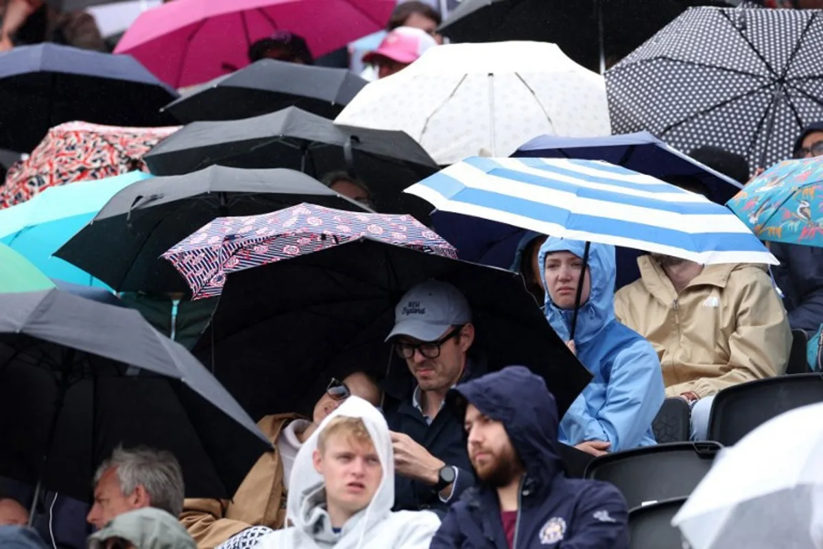 People shelter under umbrella's as a rain delay suspends the round of 32, singles match at the HSBC WTA tennis Championships at Queen's Club in west London on June 8, 2026. Adrian Dennis / AFP