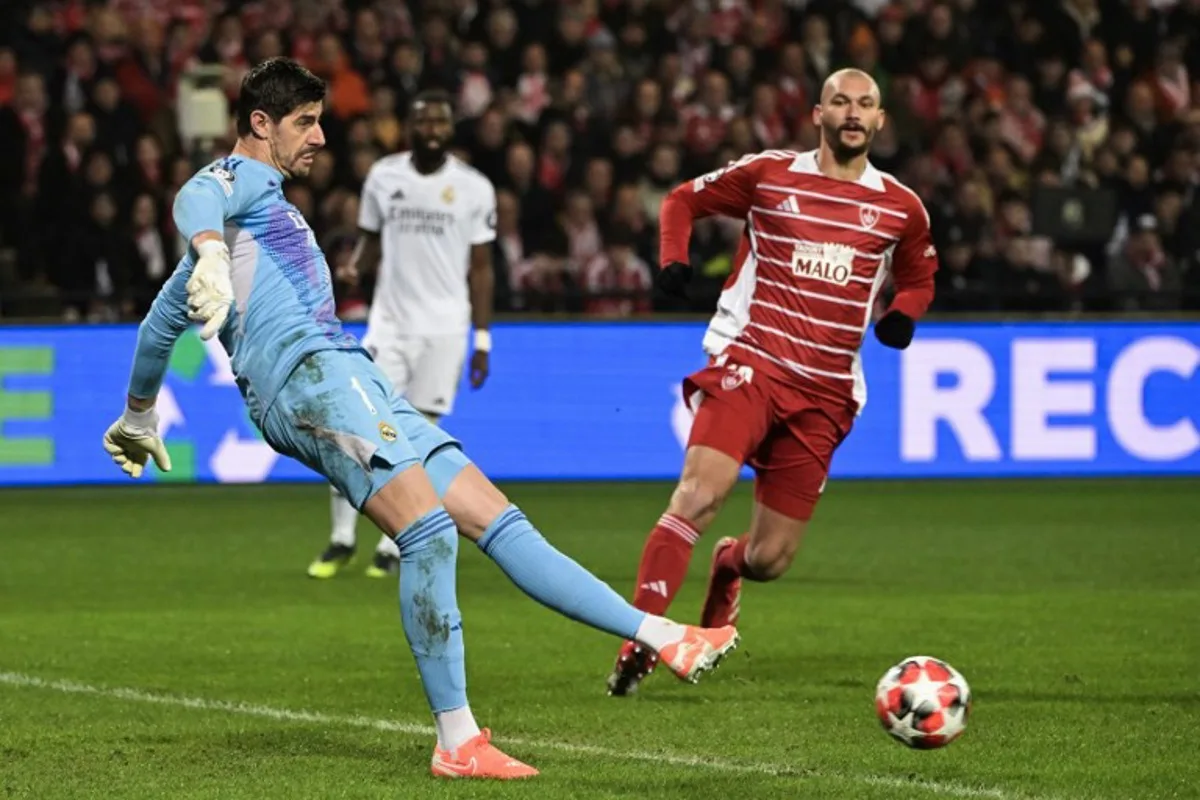 Real Madrid's Belgian goalkeeper #01 Thibaut Courtois (L) passes the ball next to Brest's French forward #19 Ludovic Ajorque during the UEFA Champions League, league phase - matchday 8 between Stade Brestois 29 (Brest) and Real Madrid CF at the Roudourou Stadium in Guingamp, north-western France, on January 29, 2025.   Damien MEYER / AFP