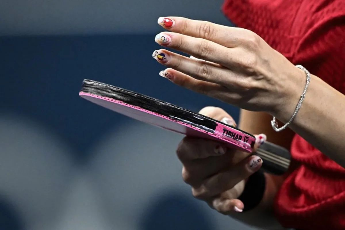 The nails of Romania's Bernadette Szocs depicting a table tennis racket, the Olympic Rings and Romania's national flag are pictured during her mixed table tennis doubles quarter-final with Romania's Ovidiu Ionescu against South Korea's Lim Jonghoon and South Korea's Shin Yubin at the Paris 2024 Olympic Games at the South Paris Arena in Paris on July 27, 2024.  WANG Zhao / AFP