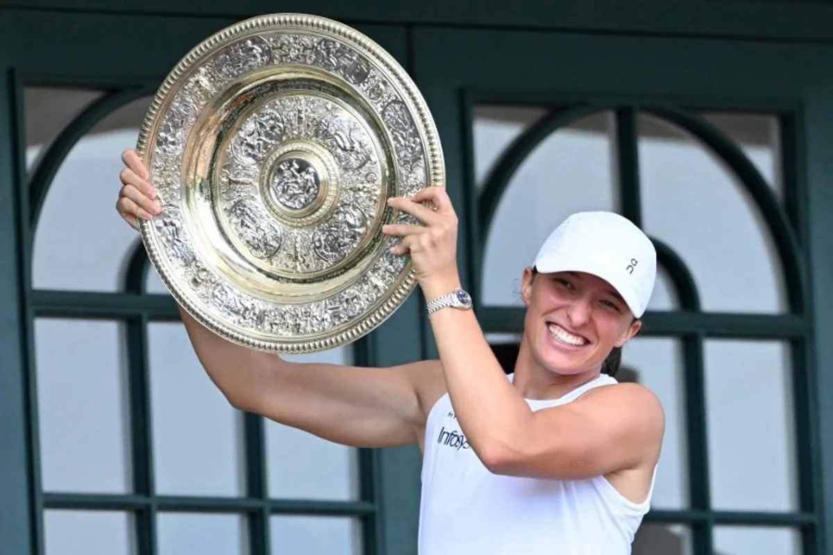 Poland's Iga Swiatek celebrates with the winner's trophy, the Venus Rosewater Dish, as she shows it to the crowd from the Centre Court balcony after winning her women's singles final tennis match against US player Amanda Anisimova on the thirteenth day of the 2025 Wimbledon Championships at The All England Lawn Tennis and Croquet Club in Wimbledon, southwest London, on July 12, 2025. Kirill KUDRYAVTSEV / AFP