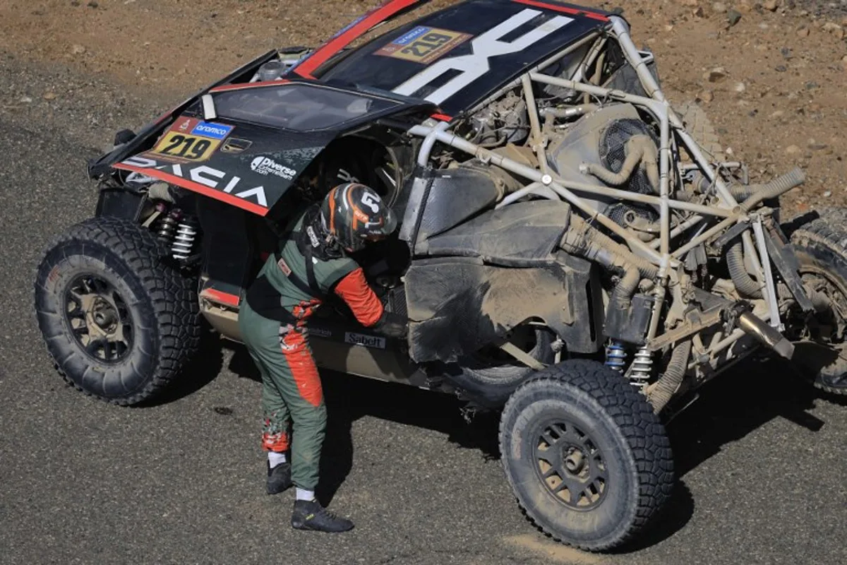 French driver Sebastien Loeb stands beside his Dacia on the road after crashing during stage 3 of the 47th Dakar Rally, between Bisha and Al Henakiyah, on January 7, 2025.  Valery HACHE / AFP