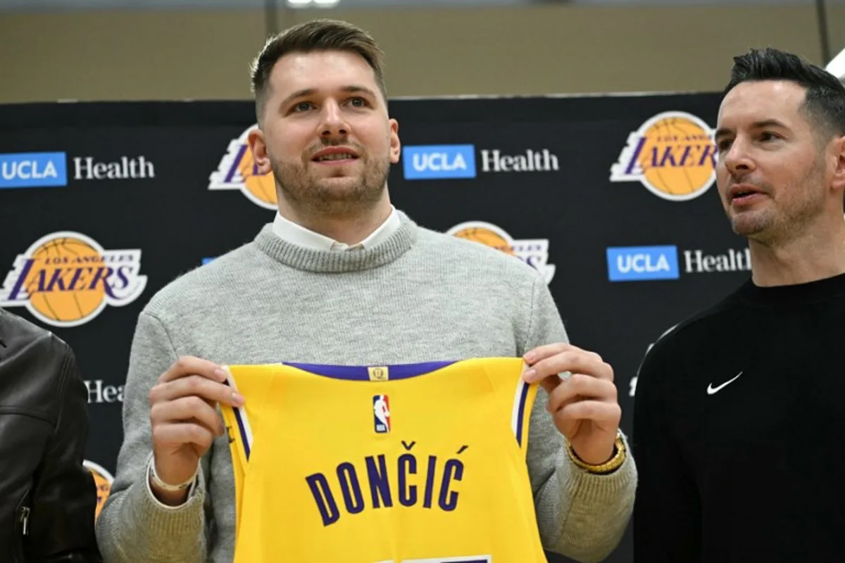 Slovenian basketball player Luka Doncic (L) holds up a jersey as he stands alongside Los Angeles Lakers head coach JJ Redick during a press conference introducing Doncic as the newest member of the Los Angeles Lakers, at the UCLA Health Training Center, in El Segundo, California on February 4, 2025. Slovenian star Luka Doncic said February 2, 2025 he thought he'd spend his entire NBA career in Dallas, thanking fans in Texas for making it feel like home a day after the Mavericks abruptly traded him to the Los Angeles Lakers. Patrick T. Fallon / AFP