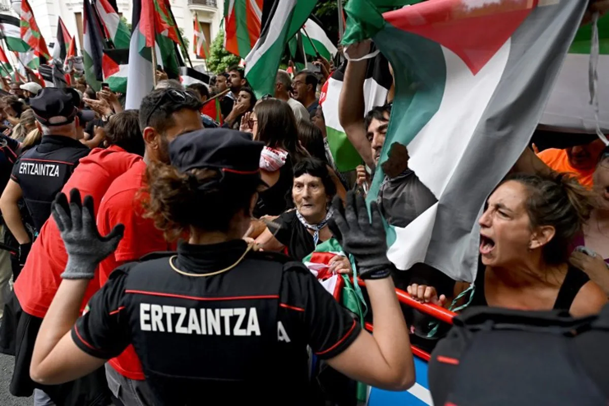 Pro-Palestinian protesters holding Palestinian flags shout as Basque regional police 'Ertzaintza' officers stand during the eleventh stage of the Vuelta a Espana cycling tour, a 167 km race from Bilbao to Bilbao, on September 3, 2025. ANDER GILLENEA / AFP